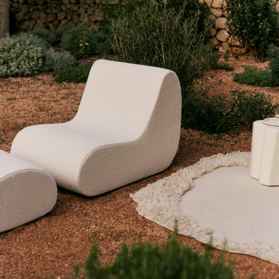 Modern outdoor chair in a garden setting with a stone wall and plants in the background