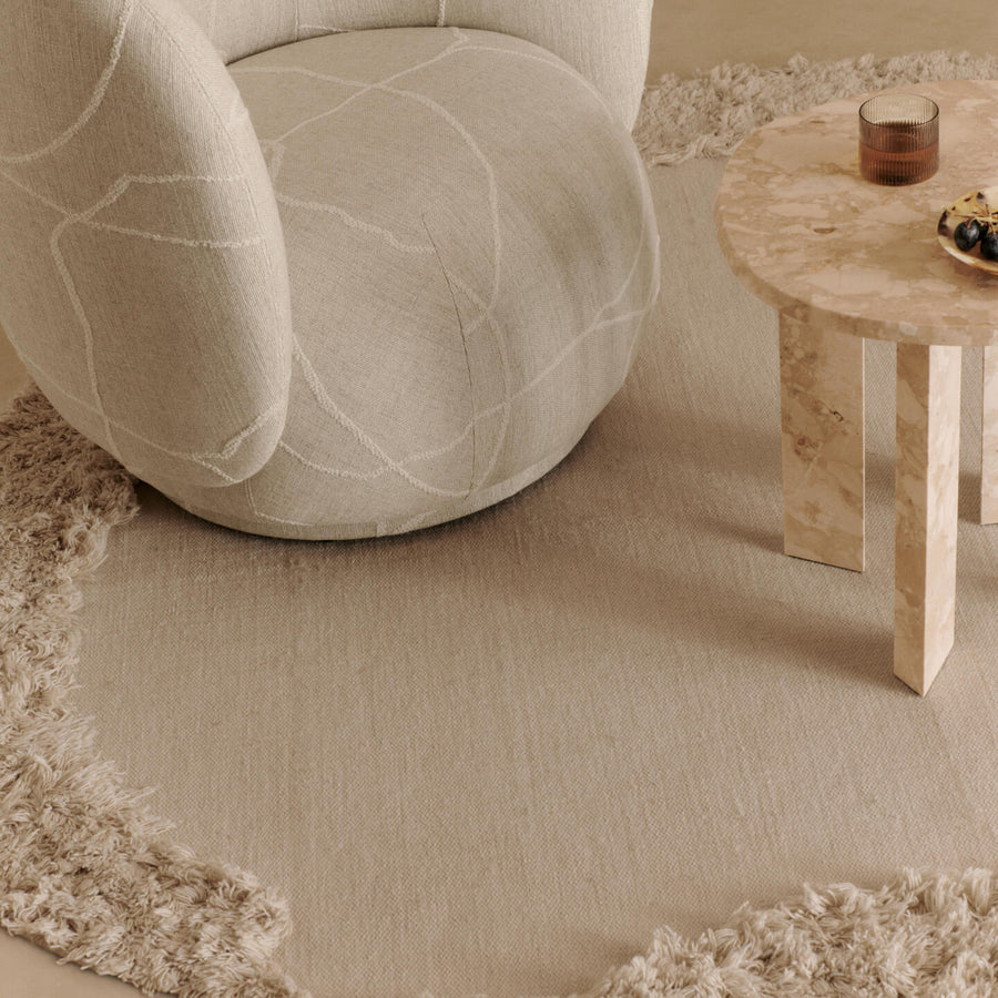 Ferm Living Beige armchair and wooden table with a textured rug in a room setting