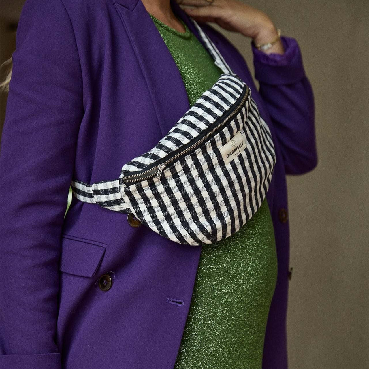 Person wearing a purple blazer and green skirt with a striped fanny pack.