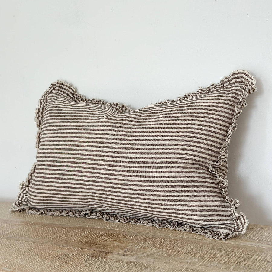 Striped pillow with ruffled edges on a wooden surface against a white wall