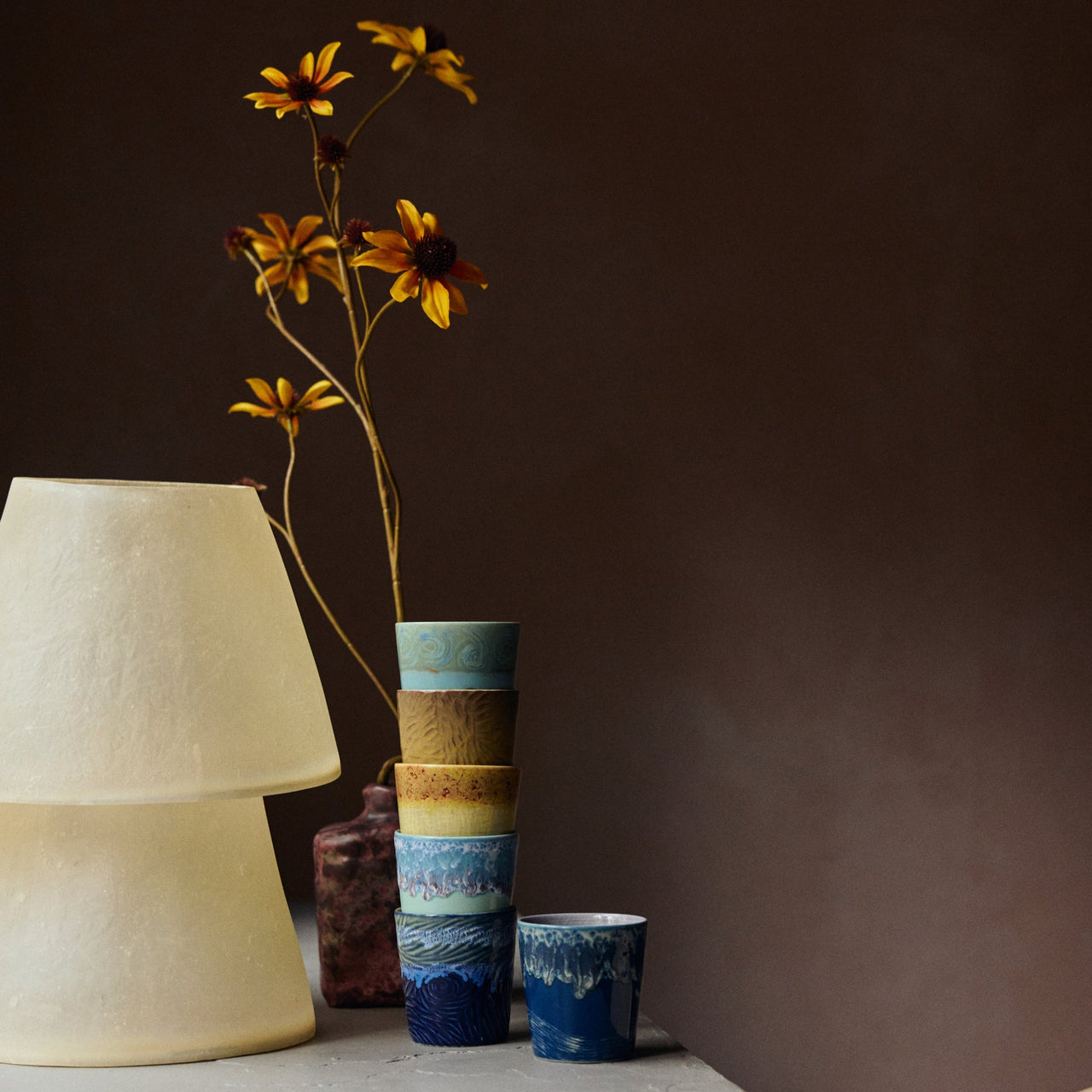 Stack of ceramic cups with a white lamp and flowers against a dark background