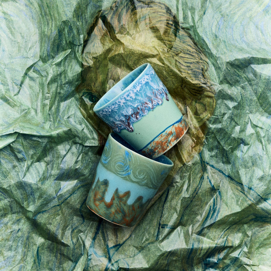 Two ceramic cups with decorative patterns on a crumpled green paper background