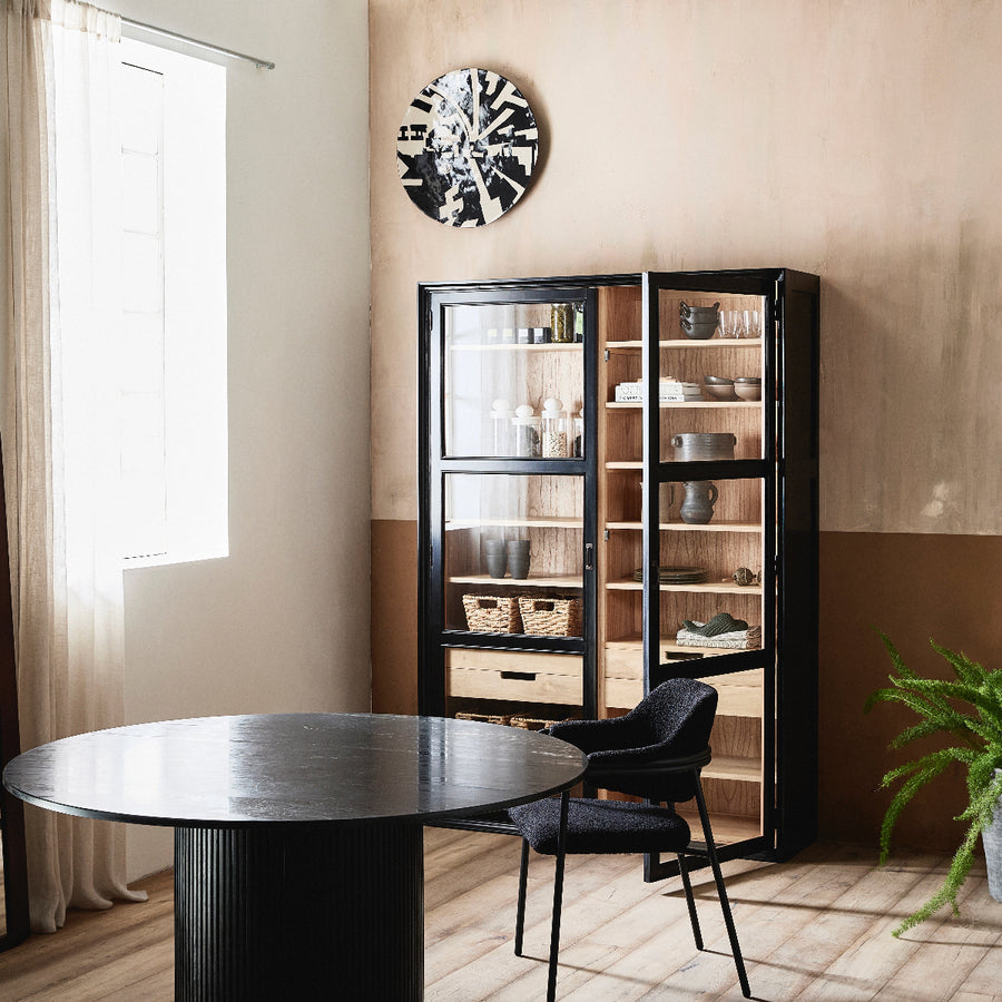 Modern interior with a round black table and chair, glass cabinet, and decorative clock.
