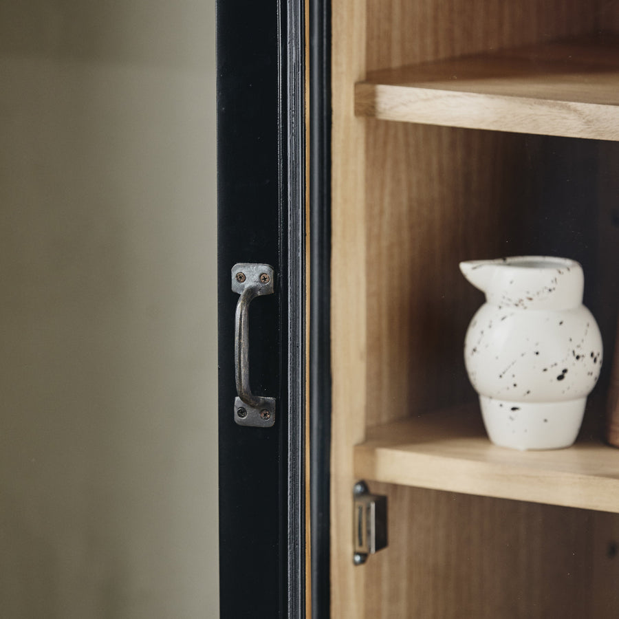Wooden cabinet with a black handle and a white speckled vase on a shelf.
