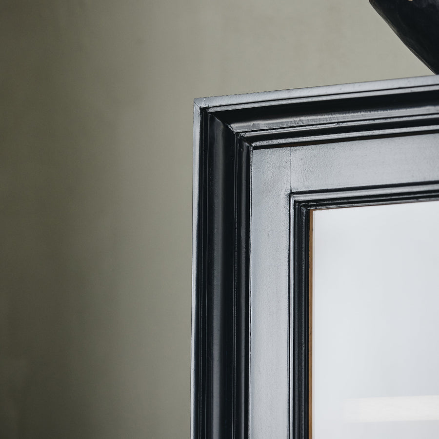 Close-up of a mirror with a black frame against a plain wall.