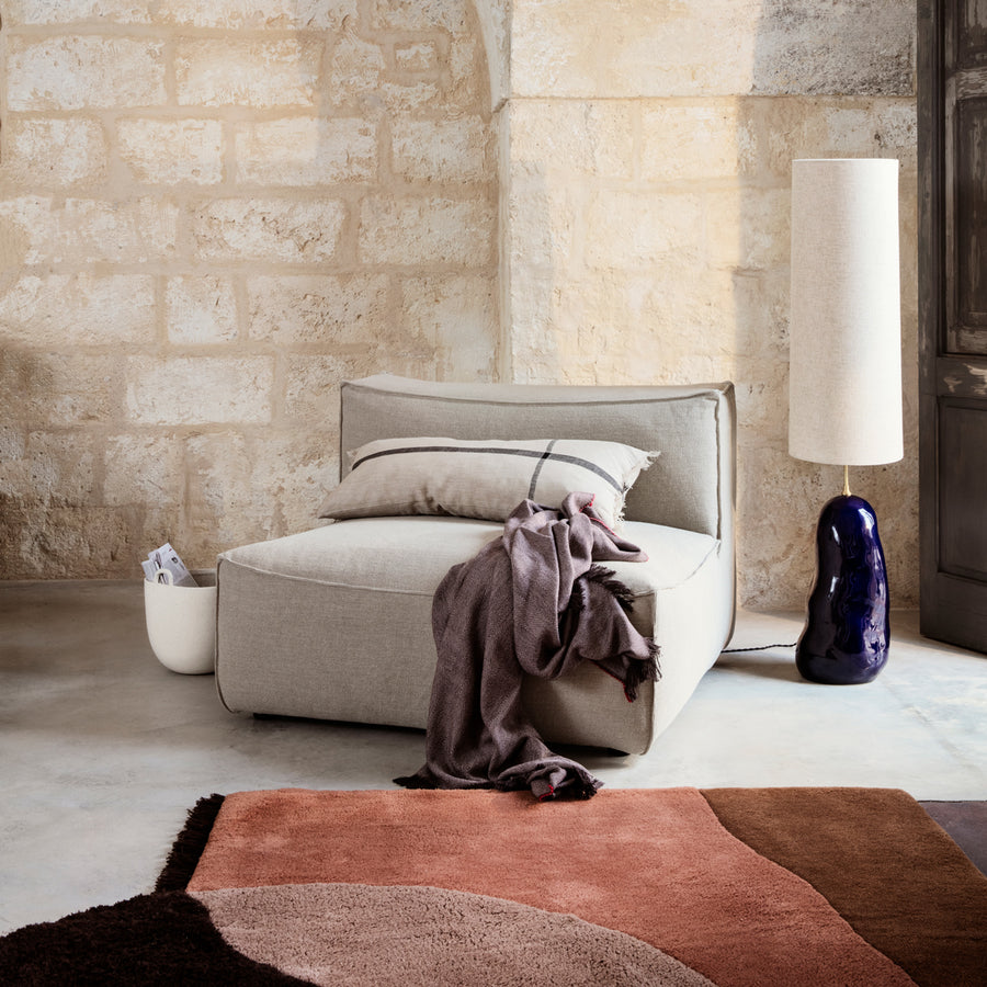 Ferm Living View Tufted Rug Red Brown Modern interior with a gray sofa, colorful rug, and decorative lamp against a stone wall.