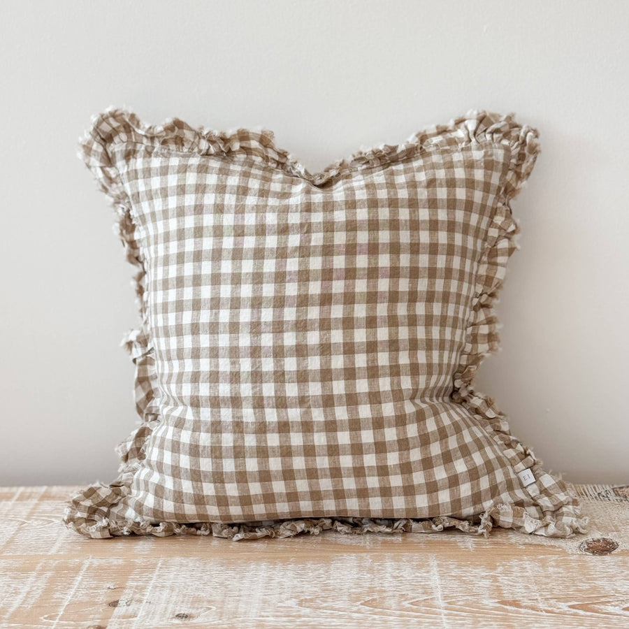 Checkered pillow with ruffles on a wooden surface against a light background