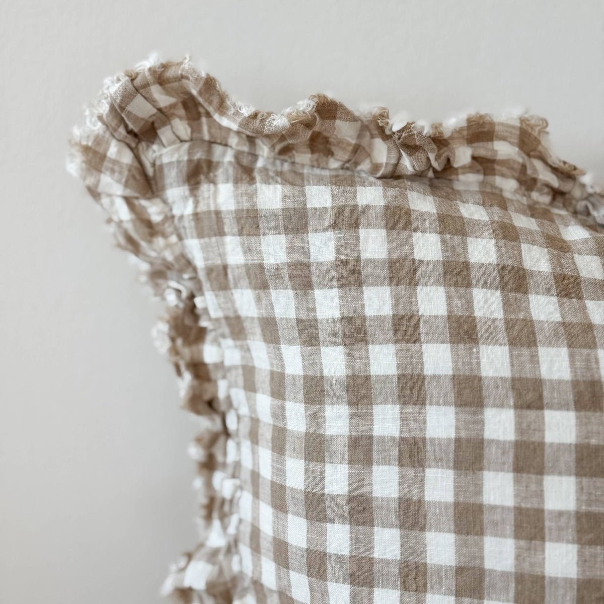 Checkered linen cushion with ruffled edges on a neutral background