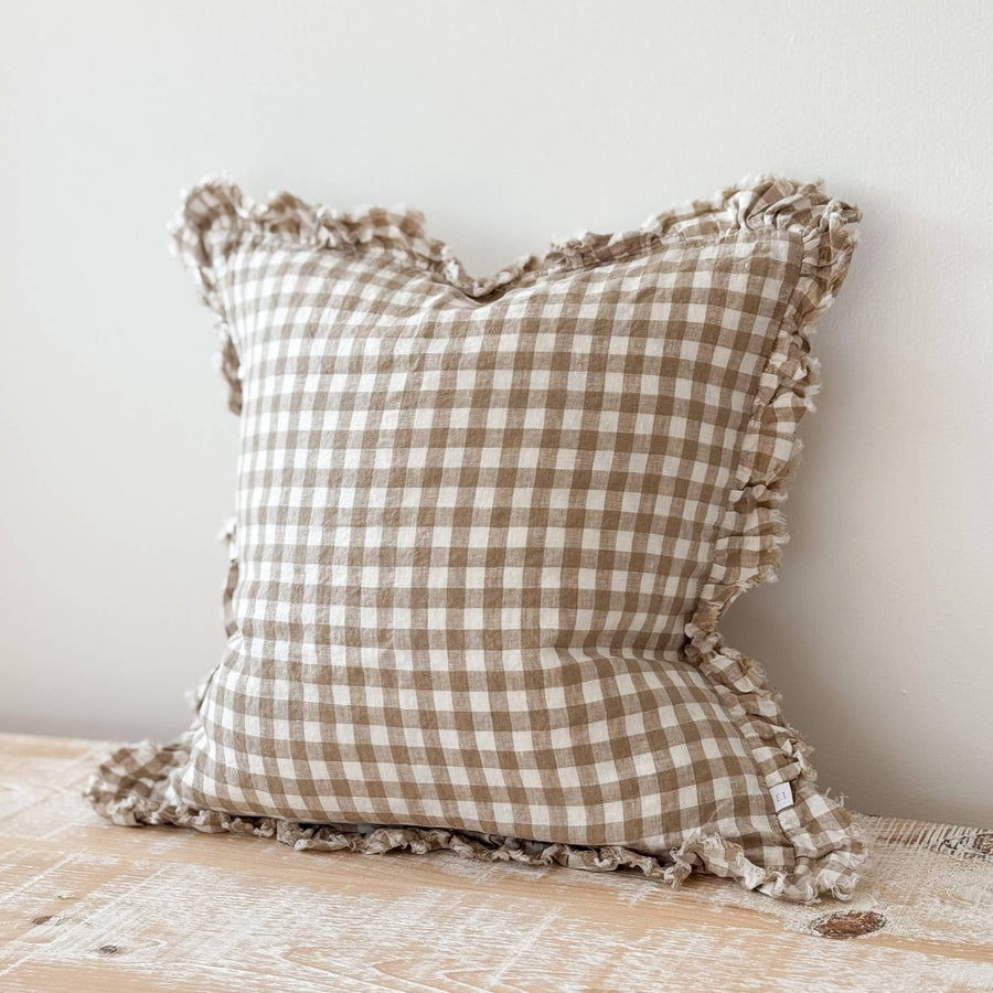 Checkered pillow with ruffled edges on a wooden surface against a white wall