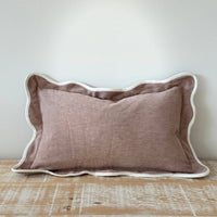 Thumbnail for Brown pillow with scalloped edge on a wooden surface against a white wall