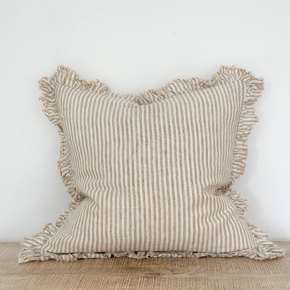 Striped linen pillow with ruffled edges on a wooden surface against a white wall