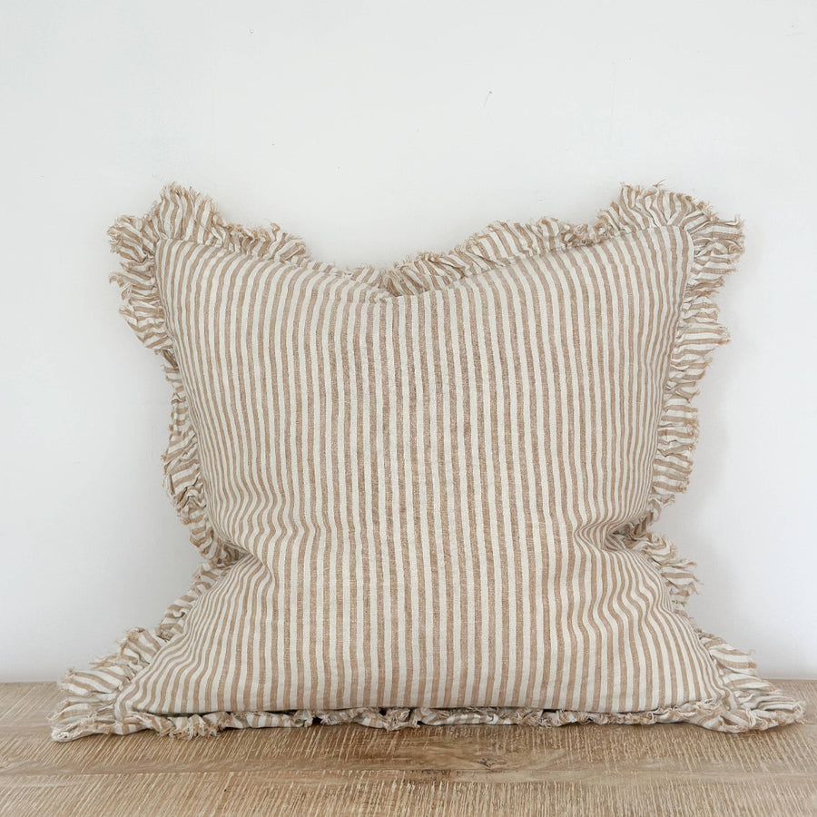 Striped linen pillow with ruffled edges on a wooden surface against a white wall