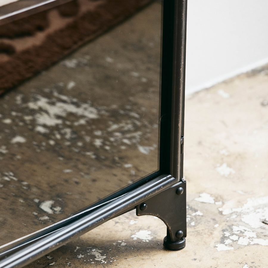 Close-up of a metal frame with a glass surface on a textured floor.