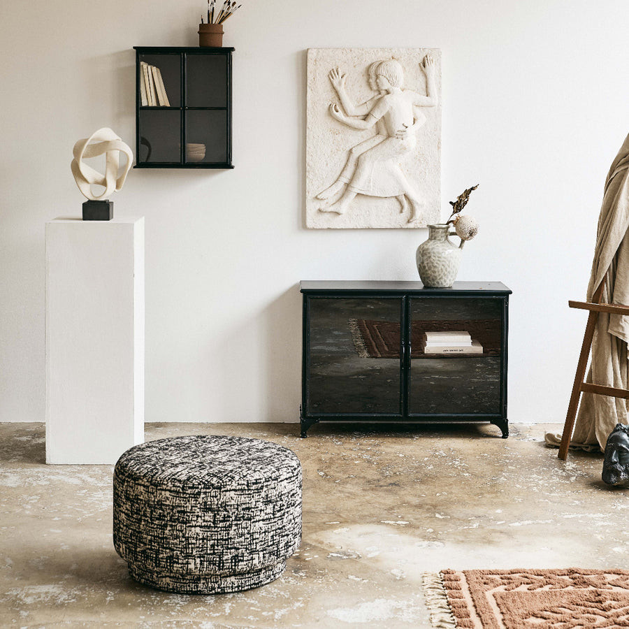 Living room with a black cabinet, patterned ottoman, and decorative items.