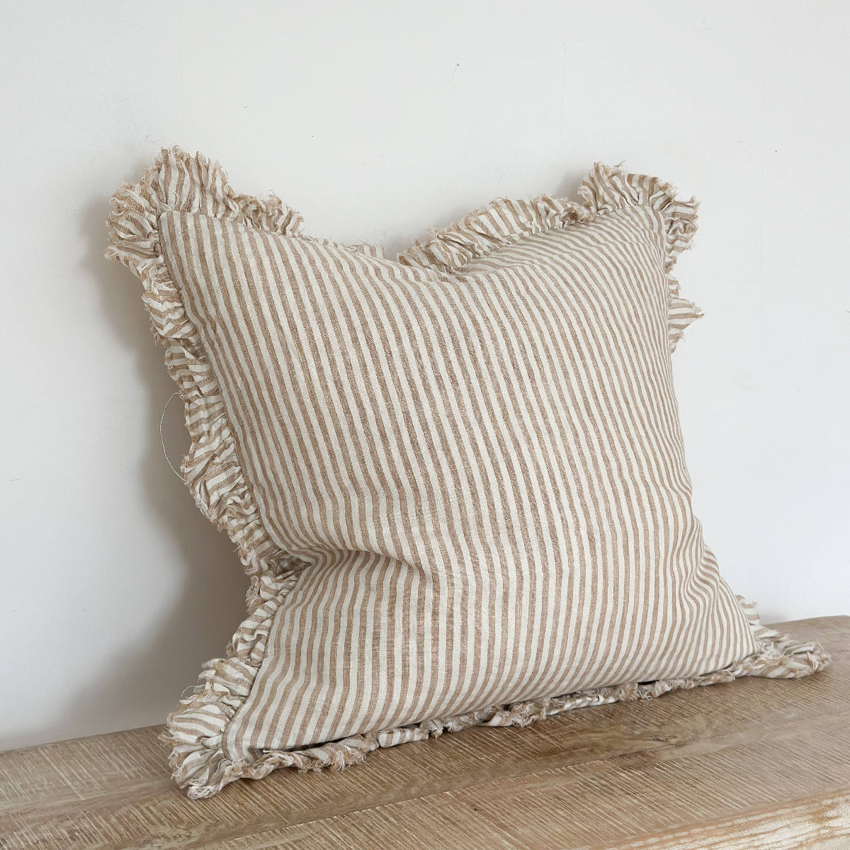 Striped linen pillow with ruffled edges on a wooden surface against a white wall