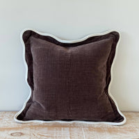 Thumbnail for Brown pillow with white trim on a wooden surface against a light gray wall