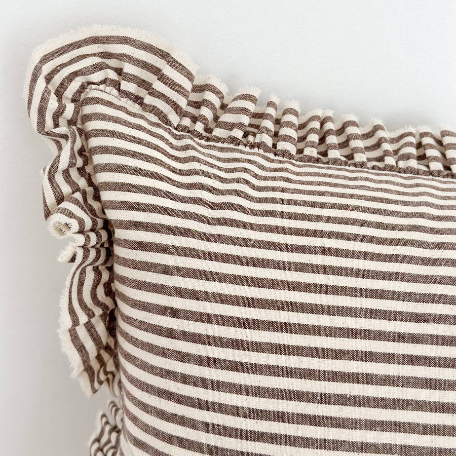 Close-up of a brown striped linen cushion with ruffled edge on a light background