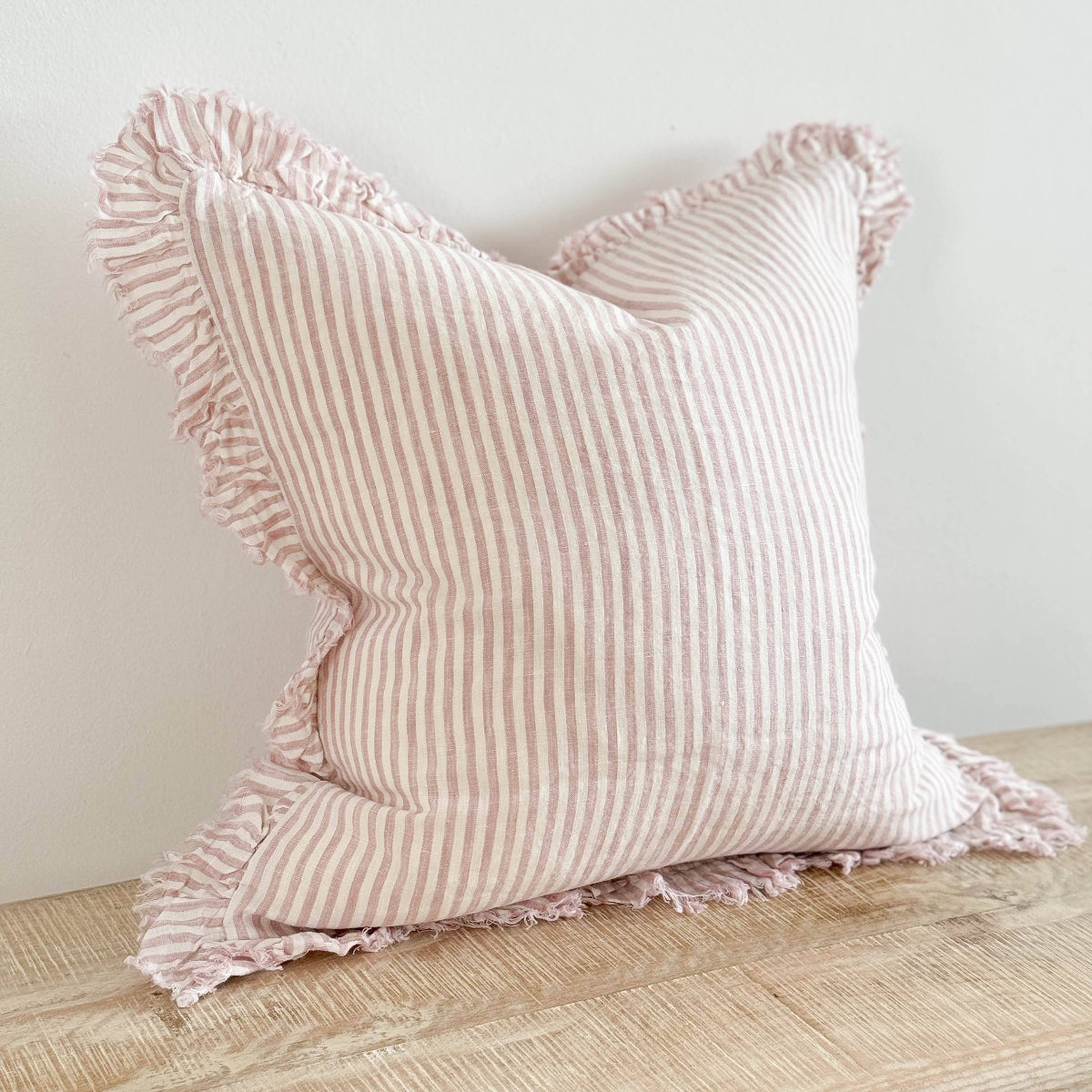 Pink striped pillow with ruffled edges on a wooden surface against a light background