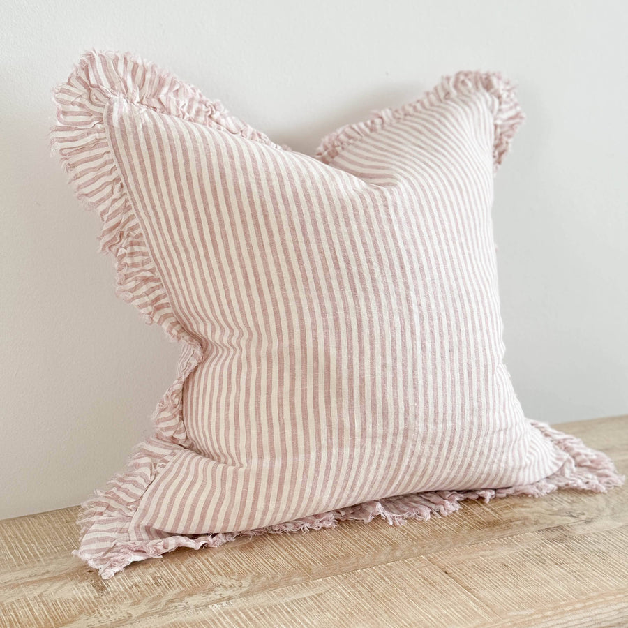 Pink striped pillow with ruffled edges on a wooden surface against a light background
