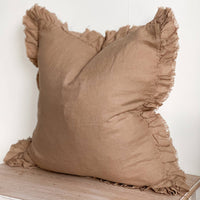 Thumbnail for Brown linen pillow with ruffled edges on a wooden surface against a white wall 
