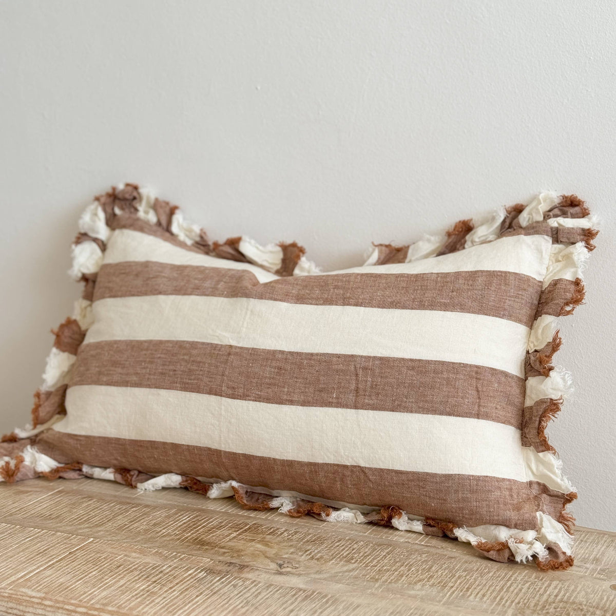Striped pillow with tassels on a wooden surface against a light gray wall