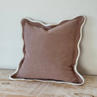 Thumbnail for Brown pillow with white trim on a wooden surface against a light wall