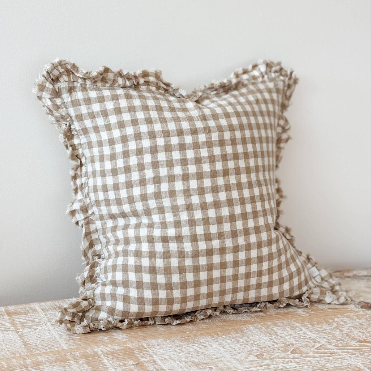 Checkered pillow with ruffled edges on a wooden surface against a white wall
