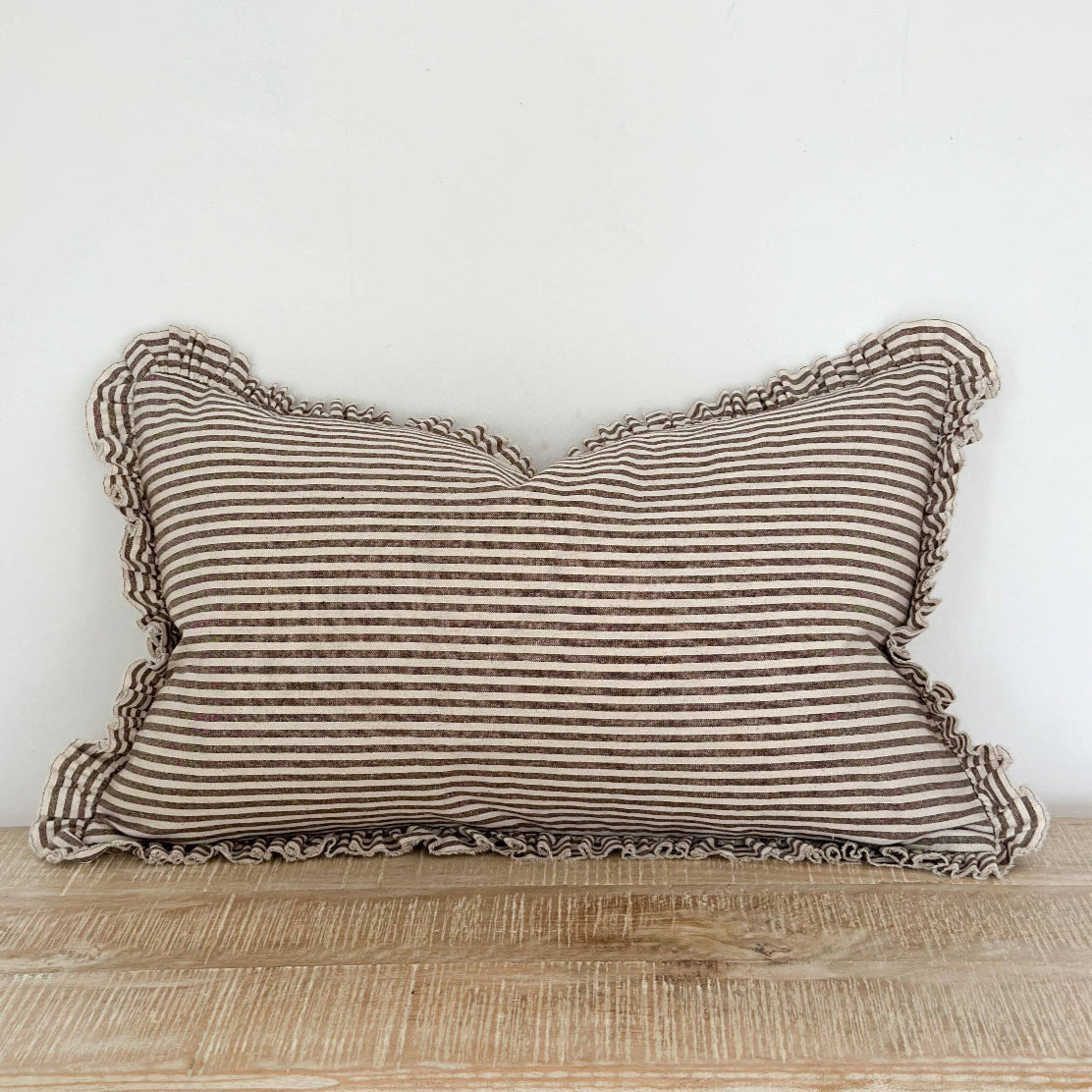 Striped pillow with ruffled edges on a wooden surface against a white wall