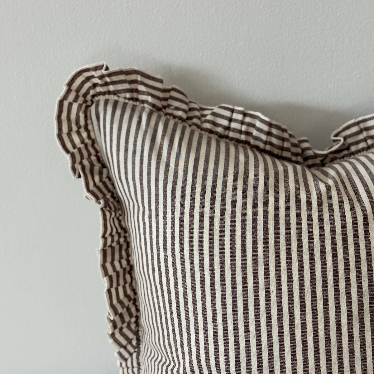 Striped pillow with ruffled edge on a neutral background