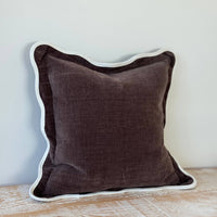 Thumbnail for Brown pillow with white trim on a wooden surface against a light blue wall