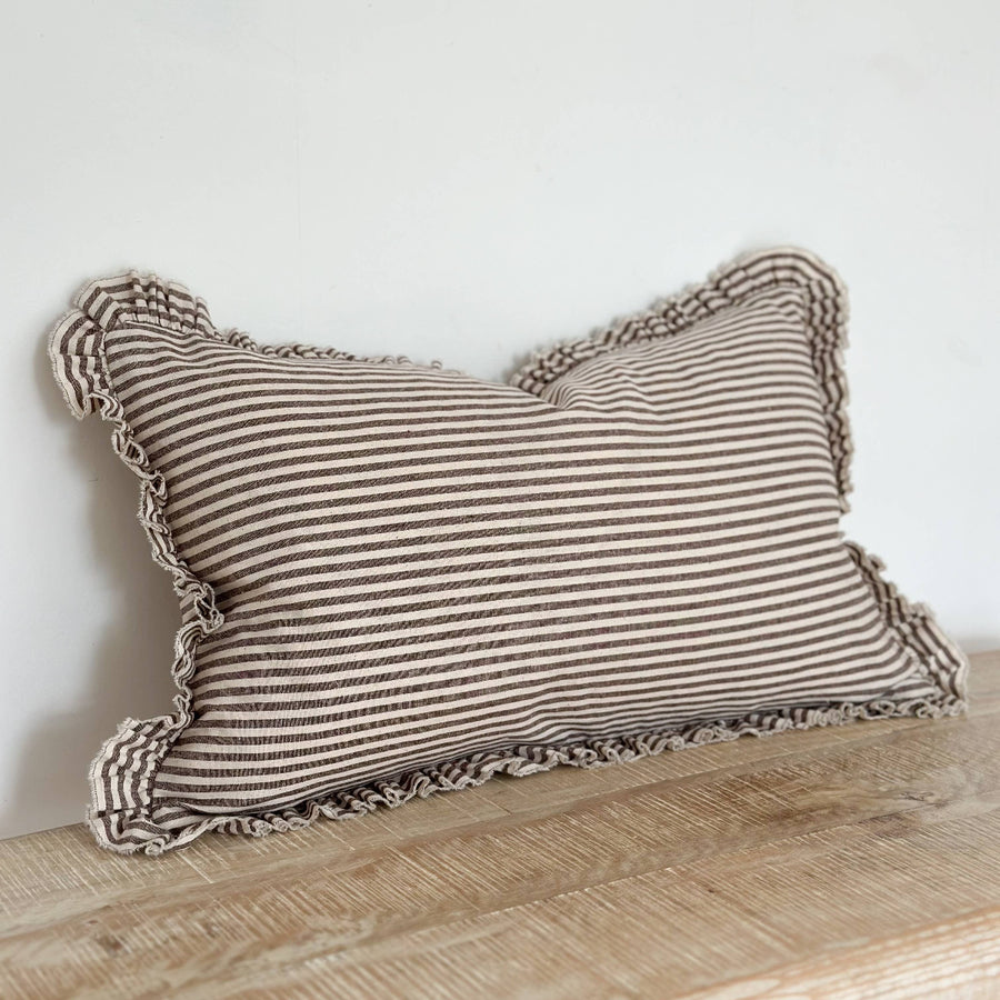 Striped pillow with ruffled edges on a wooden surface against a white wall