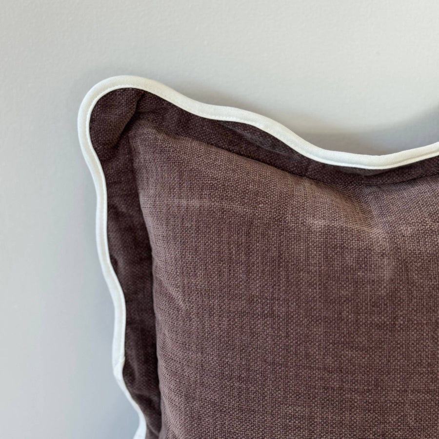 Brown textured pillow with white piping on a light gray background