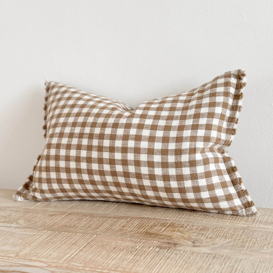 Brown and white checkered pillow on a wooden surface with a light gray background