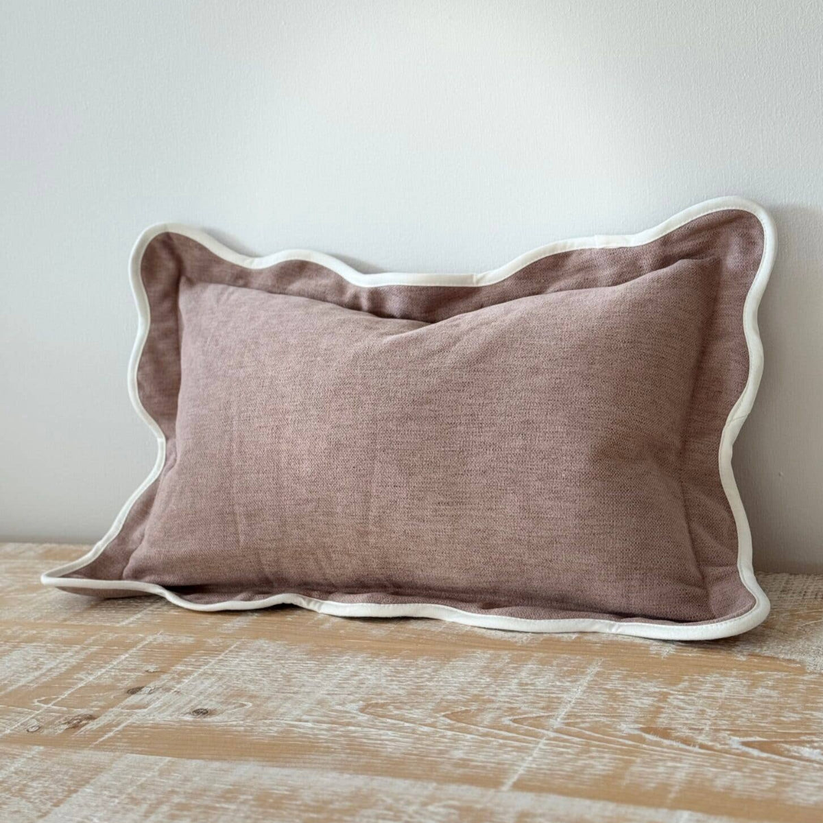 Brown pillow with white trim on a wooden surface against a light gray wall