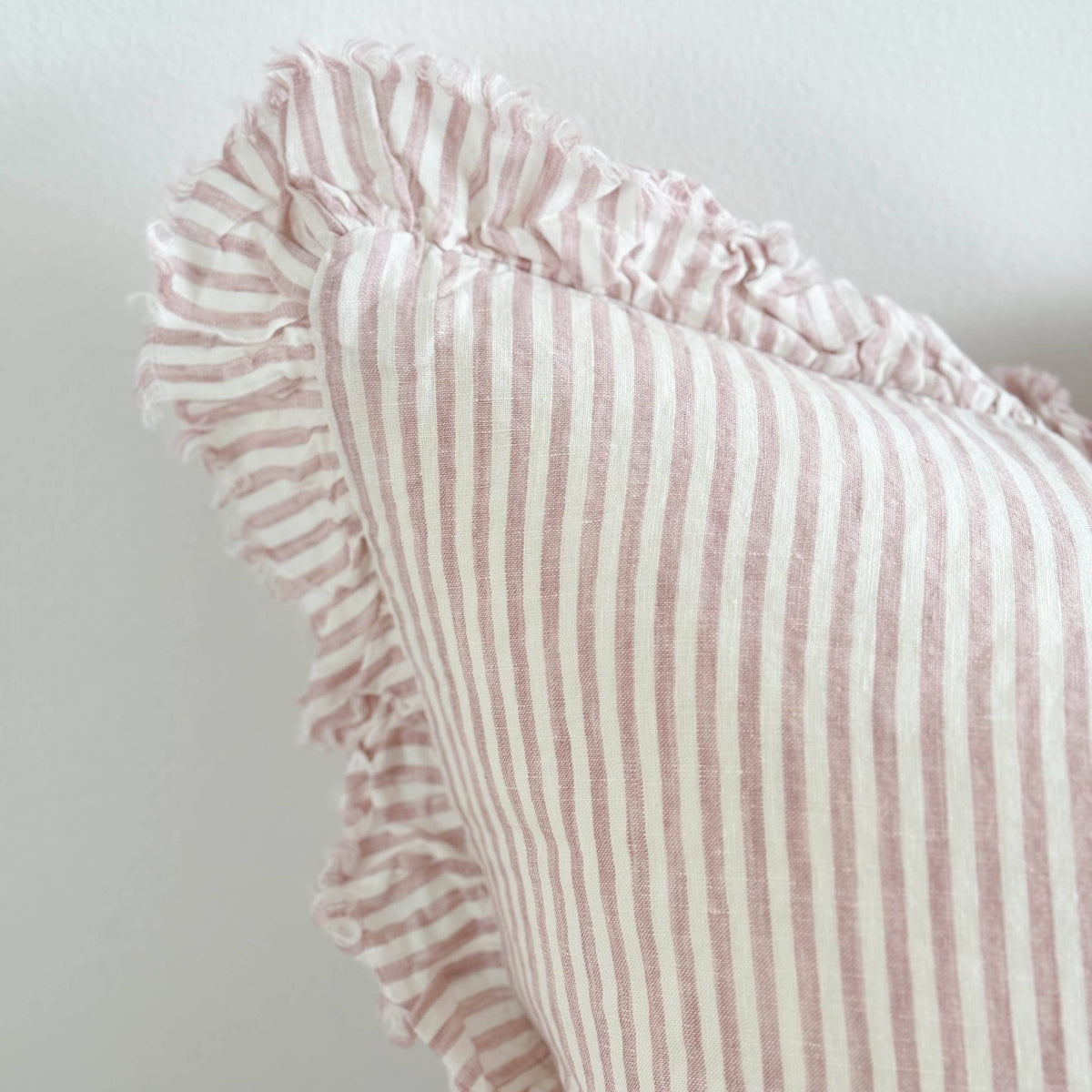 Pink striped pillow with ruffled edge on a light gray background