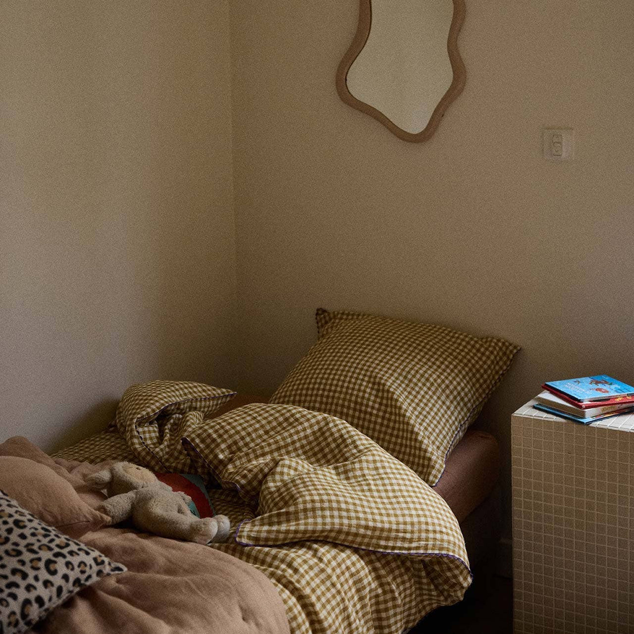 Bed with checkered blanket and pillows in a room with a mirror on the wall.