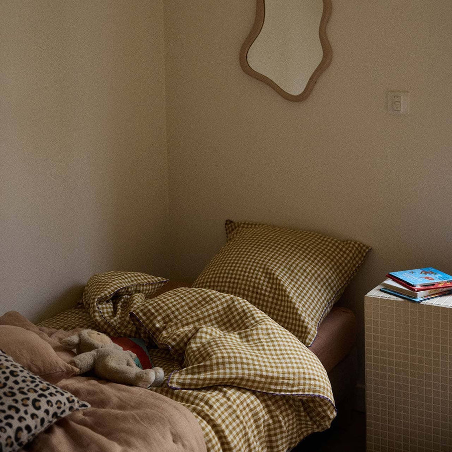 Bed with checkered blanket and pillows in a room with a mirror on the wall.