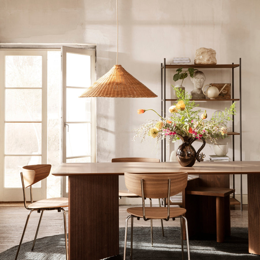 Ferm Living Dining area with wooden table, chairs, and a vase of flowers in a softly lit room.
