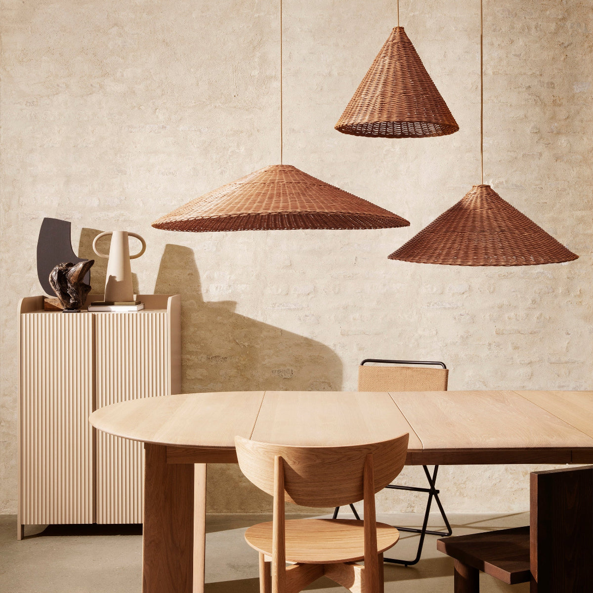 Ferm Living Dining area with wooden table, chairs, and wicker pendant lights against a textured wall.