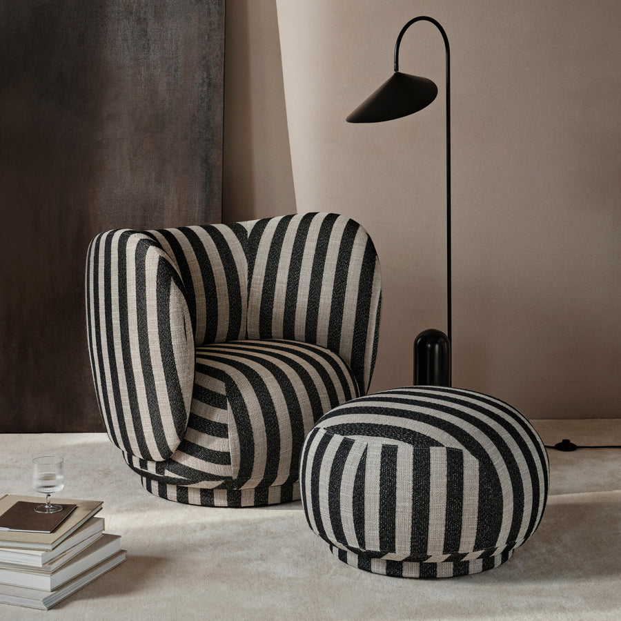 Black and white striped armchair and ottoman in a modern room setting with a lamp and books.
